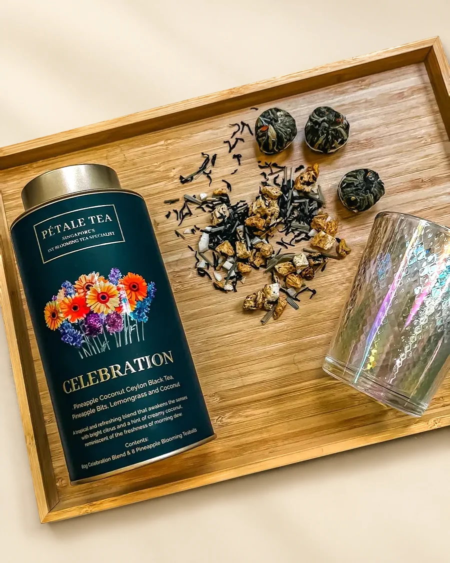 A Celebration tin with tea balls, loose tea and a glass on a bamboo tray